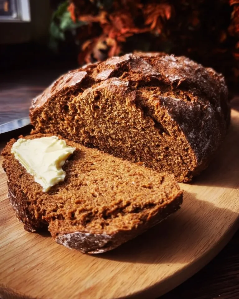 A loaf of freshly baked molasses brown soda bread on a wooden cutting board.