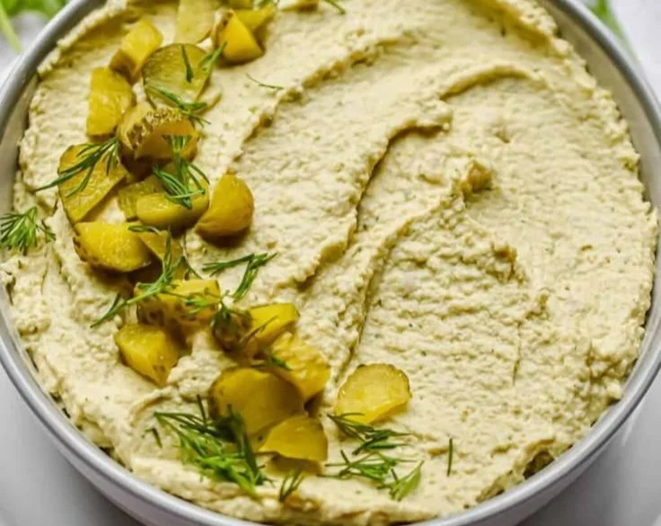 Creamy dill pickle hummus in a bowl with fresh veggies and pita bread